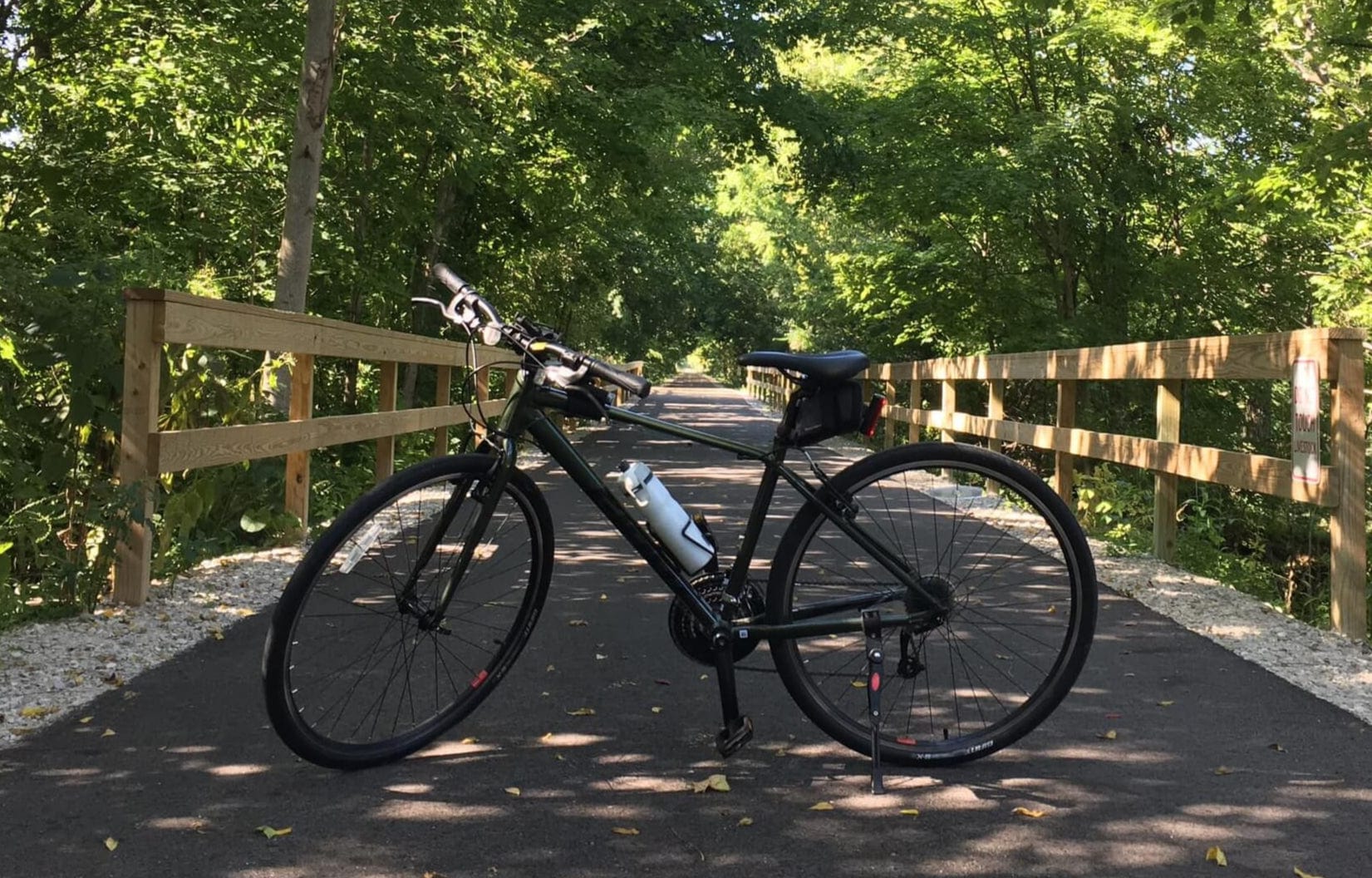 Black bicycle on a paved trail with wooden railings and trees in the background